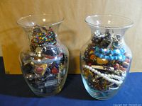 Photo shows two clear glass jars filled to the brim with assorted colorful and metallic vintage and antique wearable jewelry items.