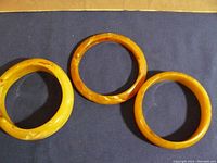 Three vintage style bangles laid on a dark cloth background showing two round bangles and one rectangular bangle in butterscotch marbled tones.
