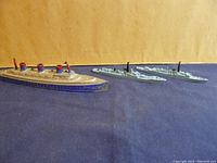 Photo showing all three metal ships on a dark blue surface against a brown background.