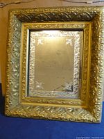 Full view of the antique mirror showing the gold embossed floral frame and the rectangular mirror glass with decorative etched corners.