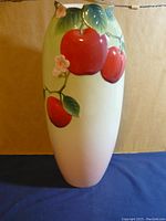 Tall porcelain vase displaying embossed design of red apples, green leaves, and pink flowers on gradient pale green to creamy white background.