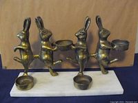Front view of the antique brass rabbit candle holder showing four standing rabbits on marble base, each holding two holders.
