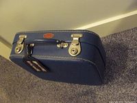 Front and top of vintage blue hardshell travel case with metal clasps and handle on carpeted floor.