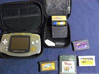 Photo of the opened carrying case showing the translucent yellow Game Boy Advance console, multiple game cartridges including Pokemon Pinball, and AA batteries.