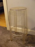 Full view of clear acrylic stool with round top and four legs, showing overall design and condition.