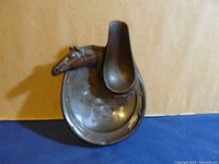 Top-down view of vintage metal pipe stand showing horse head detail and rounded base with patina and wear.