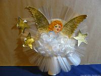 Close up of the spun cotton angel tree topper showing the orange-haired angel figure, gold wings, white cotton cloud, and gold stars.
