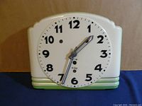 Front view of ceramic clock with white dial and black numbers and hands, white and pale green ceramic body.