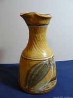 Side view of yellow-brown glazed ceramic carafe with leaf designs, showing the flared spout and textured neck.