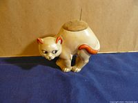 Front view of vintage ceramic spooked cat pin cushion figurine on blue cloth.