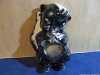 Front view of the black and white ceramic skunk wall pocket planter with a shiny glazed finish, showing the pocket opening at the belly.