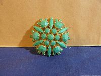 Front view of the brooch showing opaque green stones and gold-tone setting