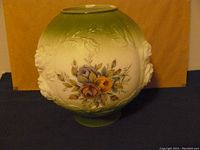 Image showing the round glass globe with green top and base, decorated with floral pattern and raised face reliefs.