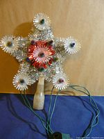 Front view of silver metal wire star tree topper with colored plastic bulb covers and frosted plastic base.