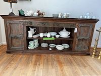Front view of vintage wooden buffet showing carved doors, center open shelves, and padded top with some dining dishes on shelves.