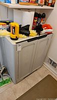 Front view of gray plastic utility cabinet with double doors and various cleaning items on top.