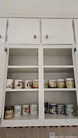 Photo showing a collection of various coffee mugs in a kitchen cabinet, featuring animal designs and travel-themed city name prints.