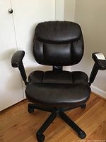 Front view of black faux leather desk chair showing padded seat and backrest, armrests, five-spoke base, and caster wheels.