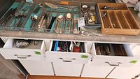 Wide view of three drawers and four organizers filled with various flatware and kitchen utensils including knives, forks, spoons, and serving tools.