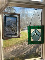 Both stained glass panels hanging in a window showing size and details.