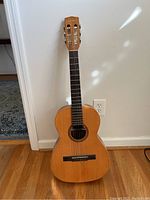 Full view of the Giannini acoustic guitar standing upright showing the wooden body with visible scratches and nylon strings.