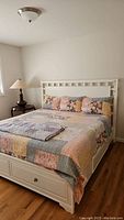Overall assembled view of white king bed frame with closed drawers and patchwork quilt