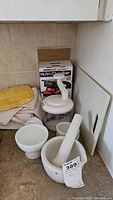 Photo showing collection of ceramic mortar and pestle, Nutri Chopper box, and kitchen towels on countertop.