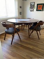 Round wooden dining table with a white marble circular Lazy Susan insert in center, shown with chairs around it in a sunlit room.