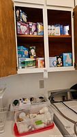 Cabinet with multiple unopened boxes of light bulbs on shelves and two plastic totes with loose bulbs on top of a washing machine.