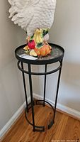 Front view of the black metal plant stand with glass top, showing the full height and leg design with a rooster figurine sitting on top (not included).