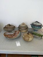 Six pottery items arranged on table including tureens, bowls, trays, and plates