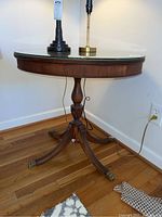 Side view of oval wooden side table with glass top, showing pedestal and brass claw feet