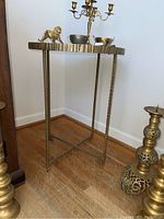 Round gold/brass colored metal framed table with a mirrored top shown with decorative small brass items on top but not included in sale.