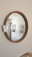 Full view of the round wooden frame mirror hanging on a wall, reflecting a room interior.