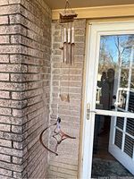 Metal wind chime with curved elements hanging from ceiling near brick wall and glass door.