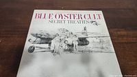 Front cover of Blue Oyster Cult Secret Treaties vinyl LP showing band members and airplane illustration with signature KH.
