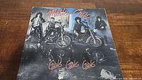 Front cover of Motley Crue vinyl record album Girls Girls Girls showing band members standing near motorcycles.