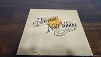Front cover of Neil Young Harvest vinyl album showing the title and artist name in stylized font on a cream colored background with some discoloration and wear visible.