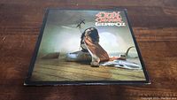 Front cover of the Ozzy Osbourne Blizzard Of Ozz vinyl album showing Ozzy reaching forward on wooden floor with arch and sunlight in background.