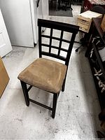 Front angled view of one wooden chair with beige cushioned seat, dark wood with grid pattern backrest, sitting on concrete floor in storage space.