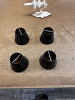 Four small black conical lamp shades placed on a flat surface, showing their tops with metal spider fitters visible for attachment to lamps.