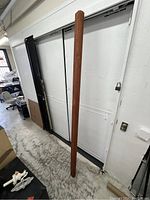 Single long wooden beam leaning vertically against a white wall, showing full length and rectangular section.