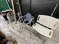 Wide view showing three assistive medical items: walker on left, commode chair center, shower stool right.