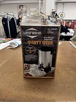 Photo of the West Bend Party Perk beverage heater box showing brand, model number 58030, capacity 12 to 30 cup, and features like lock-on lid