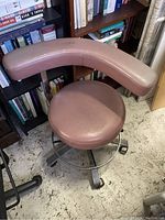 Side and front angle showing the padded round seat and curved backrest, upholstery color dusty rose, metal base with casters.