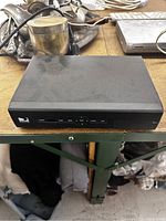 Front view of a black DirecTV set-top box player showing control buttons and indicator lights on a wooden surface.