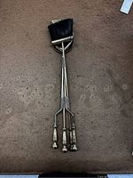 Three vintage fireplace tools laid on brown surface: broom with black bristles, poker, and tongs with wooden handles and metal shafts.