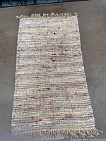 Full view of woven floor mat rug showing woven pattern in natural and muted colors with fringe on short edges.