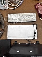 Two wired white computer keyboards and one white DVD player arranged on a brown surface.