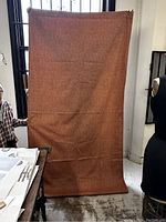 Front side of one large orange curtain with textured fabric held up in room.